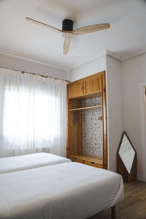 Dormitorio limpio en Hostal El Ciervo con armario de madera, ropa de cama blanca, ventilador de techo y ventana con cortinas en Villaciervos