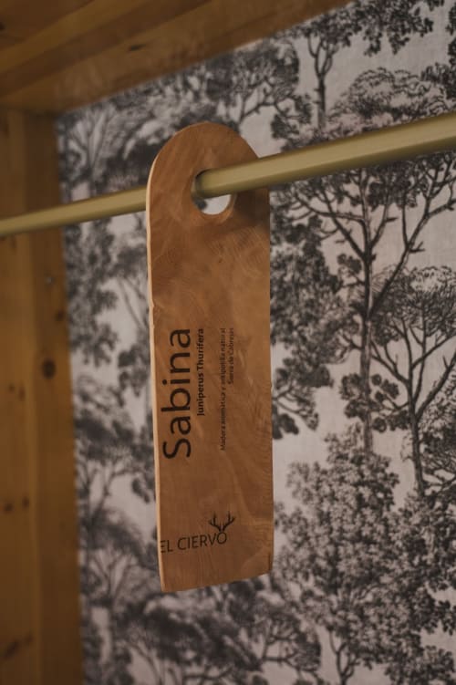 Colgador de puerta de madera para los Saltadores de Sabina en Hostal El Ciervo, con fondo de papel tapiz de bosque