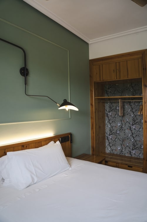 Acogedora habitación en el hostal El Ciervo con paredes verde salvia, cama de madera, ropa de cama blanca, lámpara colgante y armario.