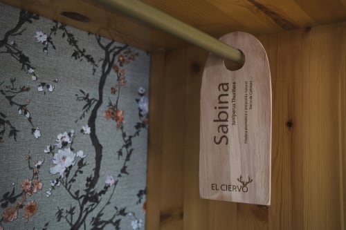 Colgador de puerta de madera con etiqueta de habitación Sabina en Hostal El Ciervo en Villaciervos con tela floral visible de fondo
