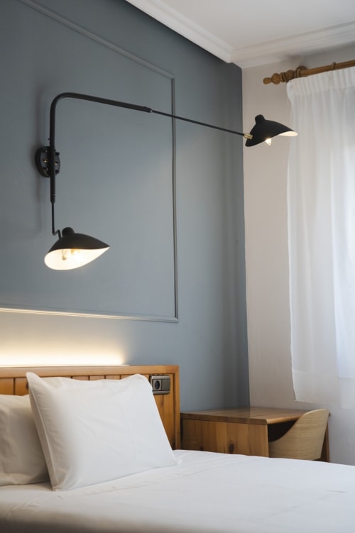 Habitación moderna del Hostal El Ciervo con cama, cabecero de madera, pared azul y lámparas articuladas negras