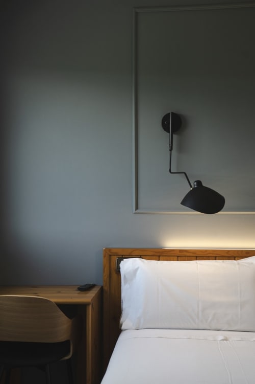 Dormitorio minimalista en Hostal El Ciervo con cama de madera, almohadas blancas, pared gris y lámpara articulada negra