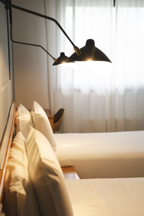 Habitación moderna en el Hostal El Ciervo con almohadas blancas, lámpara colgante negra y luz natural de la ventana
