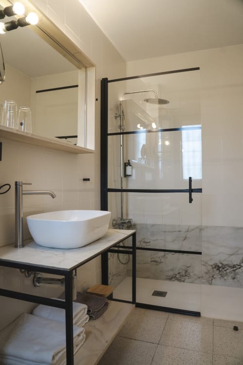 Baño moderno del Hostal El Ciervo en Villaciervos con lavamanos tipo vasija, ducha accesible, detalles en mármol y accesorios negros