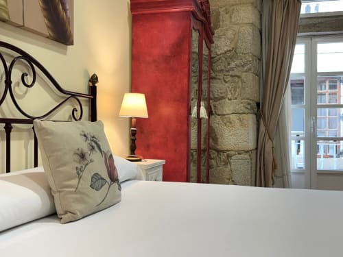 Elegante dormitorio en apartamento Vermello, Baiona con cama de hierro forjado, almohada decorativa, lámpara de mesita, pared de acento rojo y
