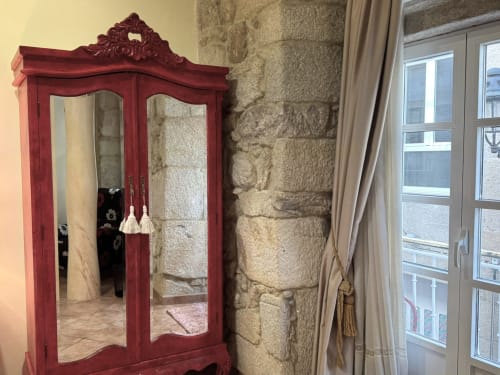 Armario rojo ornamentado con puertas espejadas en el apartamento Vermello, Baiona, con muros de piedra y vista a la ciudad
