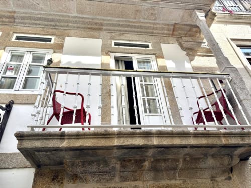 Balcón con barandillas blancas y sillas rojas en el apartamento Holibai de Baiona, vistas al centro de la ciudad