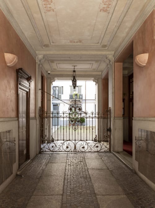 Elegante corridoio milanese con soffitto ornato, cancellata in ferro battuto e muri in terracotta presso YOUnique Boutique Rooms