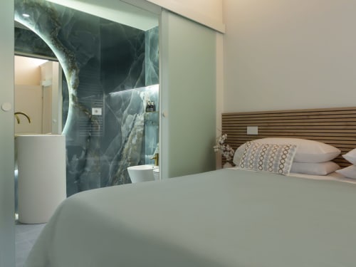 Modern bedroom at YOUnique Boutique Rooms Milano with en-suite bathroom, marble shower, wooden headboard, and city view