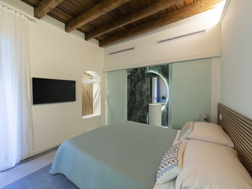 Camera moderna presso YOUnique Boutique Rooms Milano con travi a vista, TV schermo piatto e bagno ensuite con piastrelle verdi
