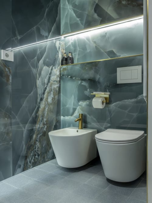 Modern bathroom at YOUnique Milano with marble walls, white bidet and toilet, brass fixtures, and lit mirror