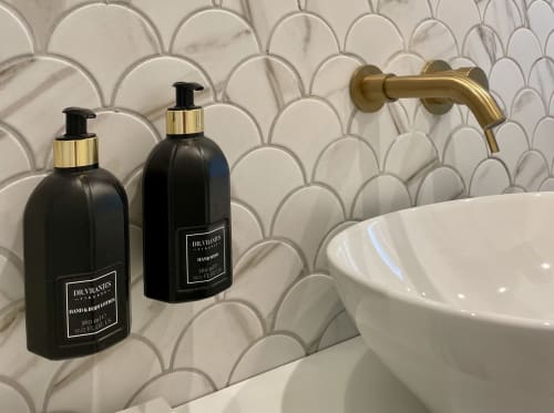 Lussuosi accessori bagno presso YOUnique Boutique Rooms Milano: flaconi Dr. Vranjes neri e rubinetto dorato su piastrelle a conchiglia.