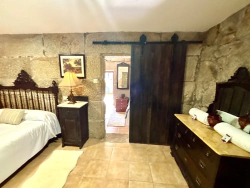 Dormitorio de villa histórica en Baiona con muros de piedra, muebles de madera oscura y decoración tradicional