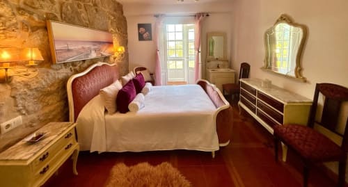 Dormitorio elegante en villa Holibai de Baiona con muebles antiguos, muros de piedra y vistas al jardín