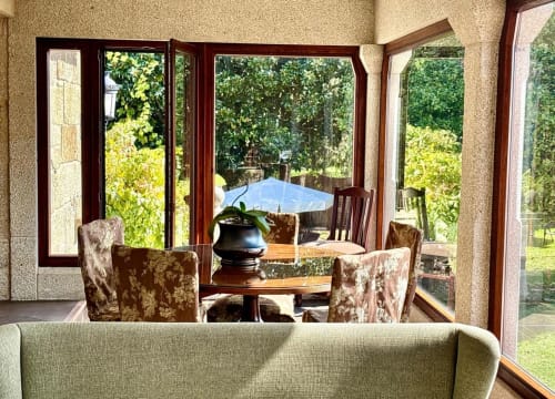 Vista del interior de villa soleada con puertas abiertas hacia jardines exuberantes, Baiona