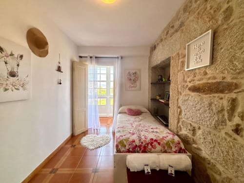 Dormitorio con encanto en villa histórica, pared de piedra, cama individual con ropa de cama floral, suelo de terracota y puerta con vista al jardín