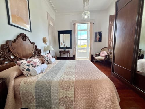 Elegante dormitorio en villa histórica de Baiona con cama de madera ornamentada, vistas al jardín y muebles de época