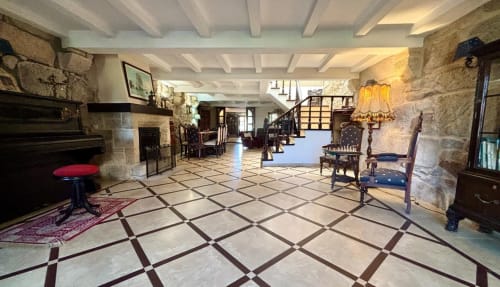 Sala de estar de villa histórica en Baiona con muros de piedra, chimenea, suelo de baldosas, vigas de madera, muebles de época y jardín