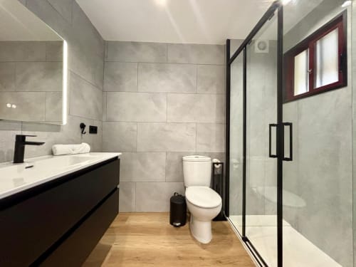 Baño moderno en apartamento Meiga do Mar, Baiona con tocador negro, ducha con mamparas de cristal y vistas al mar