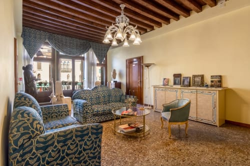 Elegante soggiorno palazzo veneziano con arredi damascati blu, soffitto con travi a vista, lampadario e viste sulla città a Palazzo