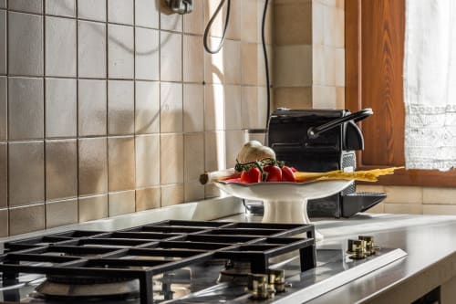 Cucina lussuosa in cottage stile palazzo veneziano con fornello a gas, piani di lavoro bianchi, rivestimento in piastrelle, pomodori freschi e vista sul mare
