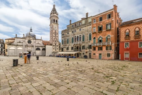 Piazza veneziana con campanile storico, edifici rinascimentali colorati e piccioni a Venezia, Italia