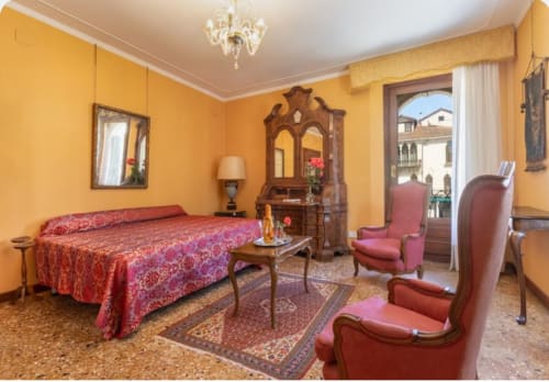 Camera da letto di lusso in palazzo veneziano con pareti gialle, letto damascato rosso, mobili in legno e vista mare dai balconi.