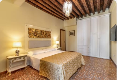 Camera da letto lussuosa con travi in legno a vista, guardaroba bianco e biancheria dorata a Palazzo San Firmino a Venezia