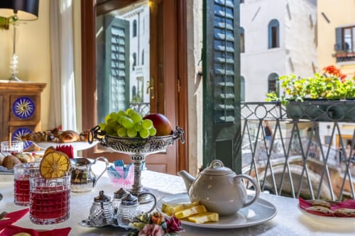 Colazione elegante al Palazzo San Firmino con frutta fresca, teiera e vista sui canali veneziani dal balcone