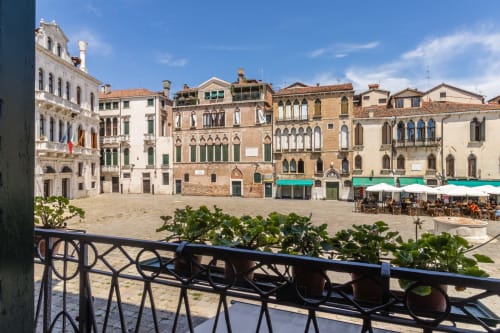 Affascinante piazza veneziana con eleganti palazzo, persiane verdi e caffè all'aperto affacciato sull'acqua a Venezia