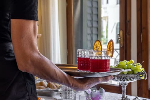 Cameriere con cocktail rosso guarnito di fettine di limone al Palazzo San Firmino Venezia, acini d'uva verde visibili