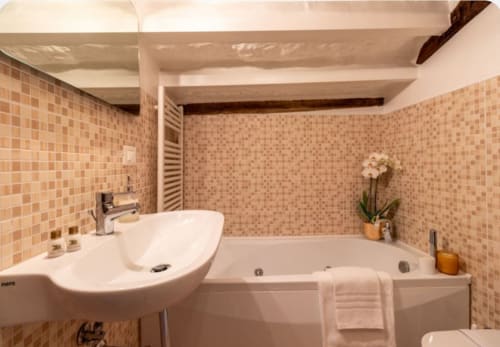 Bagno dai toni caldi con piastrelle a mosaico beige, lavabo bianco, vasca da bagno e orchidea in vaso al Palazzo San Firmino, Venezia