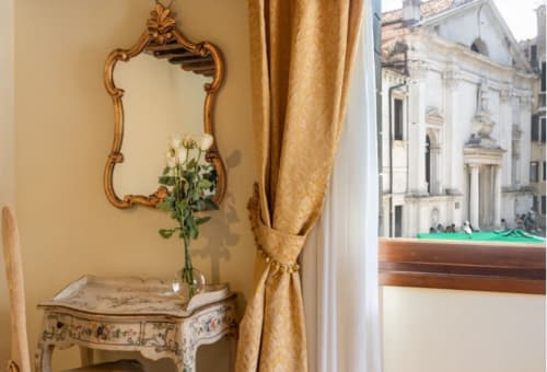 Specchio dorato ornato e scrivania dipinta in una camera veneziana che affaccia sul canale e sull'architettura storica
