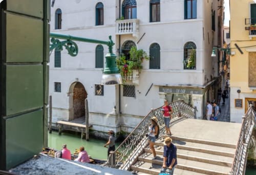 Canale veneziano con palazzo bianco storico, acqua verde, turisti sul ponte e architettura italiana tradizionale