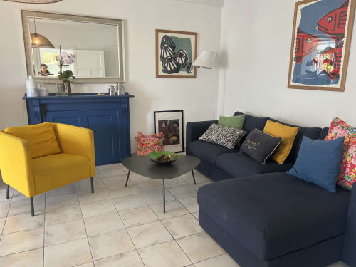 Séjour lumineux aux Gîtes De L'odet avec fauteuil jaune, canapé foncé et manteau de cheminée bleu