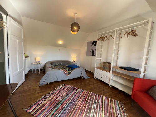 Chambre spacieuse aux Gîtes De L'odet avec lit, armoire, tapis coloré et coin détente rouge à Clohars-Fouesnant