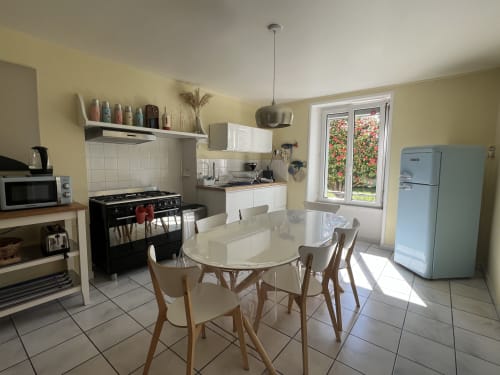 Cuisine-séjour lumineux du gîte Les Gîtes De L'odet avec électroménagers blancs, table ronde et vue sur le jardin