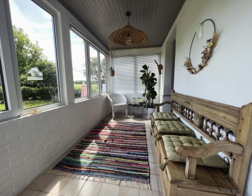 Véranda lumineuse des Gîtes De L'odet avec vue sur jardin, suspension en osier, tapis rayé, banquette verte rembourrée