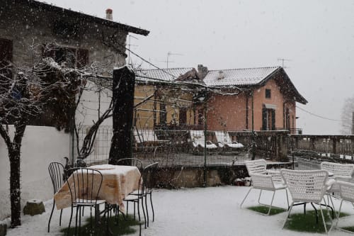 Snowy mountain courtyard at THE V Collection Sormano with dining chairs and rustic buildings during winter snowfall