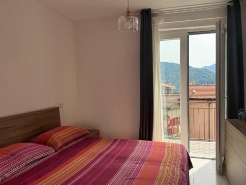 Camera da letto luminosa con biancheria a righe rosse, vista montagne dal balcone, appartamento Sormano presso THE V Collection hotel in Italia