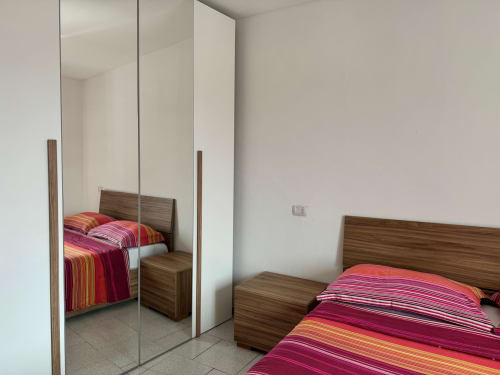 Camera da letto moderna con armadio a specchi, biancheria da letto a righe colorate, mobili in legno - Appartamento Sormano 2