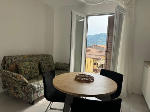 Moderno soggiorno con divano decorato, tavolo da pranzo e balcone aperto che affaccia sulle montagne di Sormano