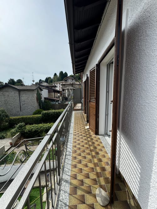 Corridoio coperto esternamente dell'Appartamento Sormano 2 presso THE V Collection, con pavimentazione in piastrelle, porte in legno e vista sul villaggio di montagna