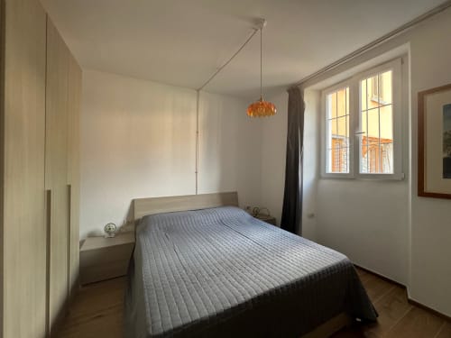 Camera luminosa dell'appartamento a Sormano con letto matrimoniale, armadio in legno, lampada a sospensione e vista montagna