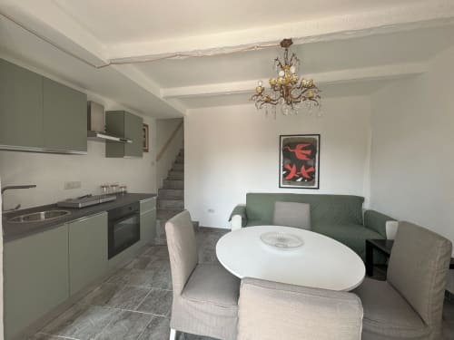 Zona living e cucina open space nell'appartamento di Sormano con divano verde, tavolo da pranzo e cucina moderna