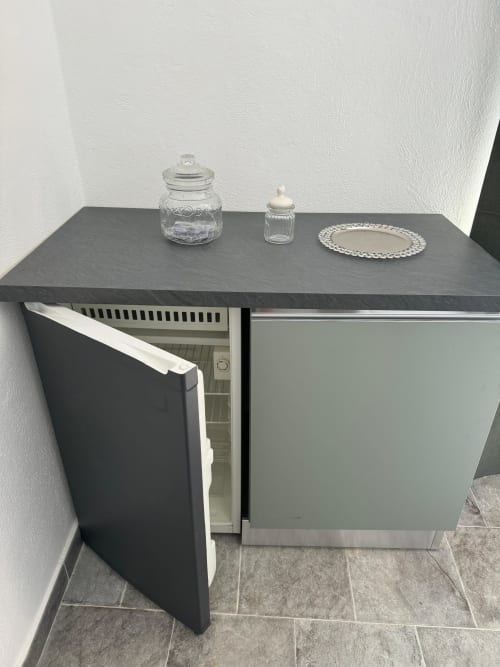 Piccola cucina buia con frigorifero aperto e barattoli di vetro sul bancone nell'appartamento di Sormano