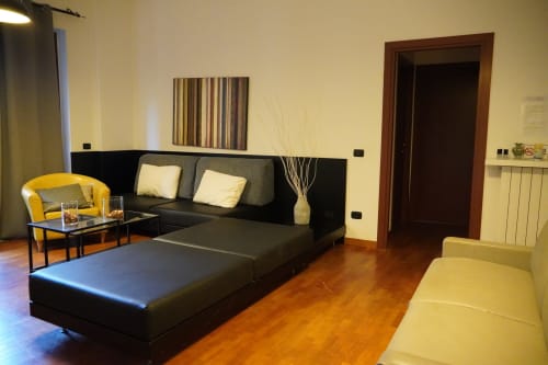 Soggiorno moderno Roma 2 con divano nero, poltrona gialla e pavimenti in legno presso THE V Collection, Turate