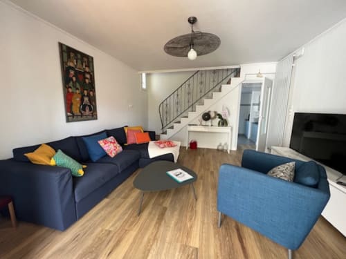 Séjour lumineux des Gîtes De L'odet avec canapé bleu marine, fauteuil bleu, parquet et accès escalier.