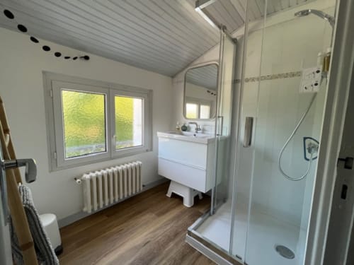 Salle de bains moderne avec douche vitrée, meuble blanc, radiateur chauffant, parquet et vue sur le jardin