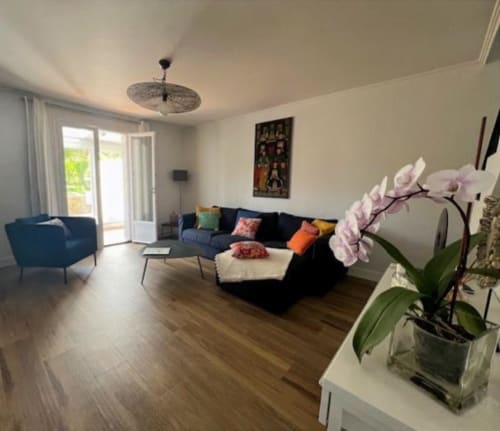 Salon de gîte moderne avec canapé gris anthracite, fauteuil bleu, orchidée et vue sur le jardin aux Gîtes De L'odet
